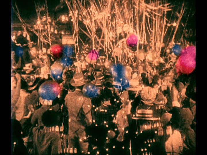 Yellow-tinted overhead long shot of a crowd that features blue and red balloons