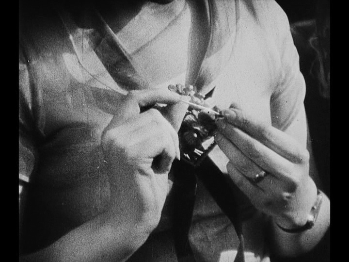 Close-up of Mary testing the sharpness of a brooch pin with her finger