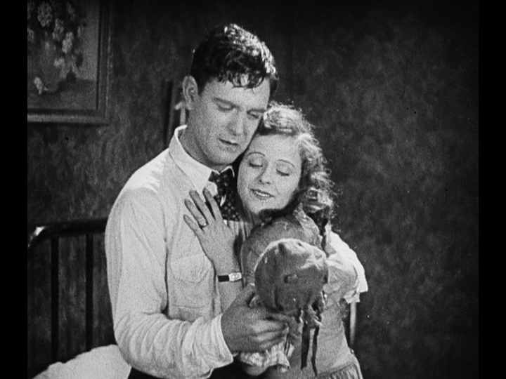 Medium shot of Jim and Mary looking at her doll as they embrace