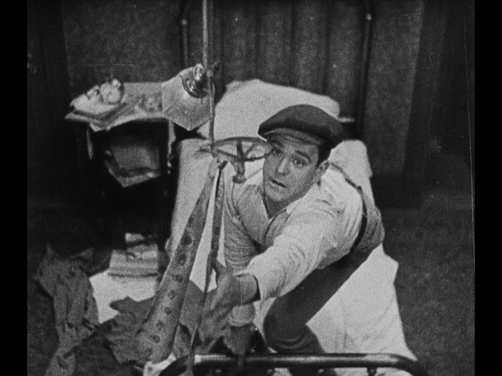 Overhead medium shot of Jim reaching for the tie which hangs from a light fixture in his apartment