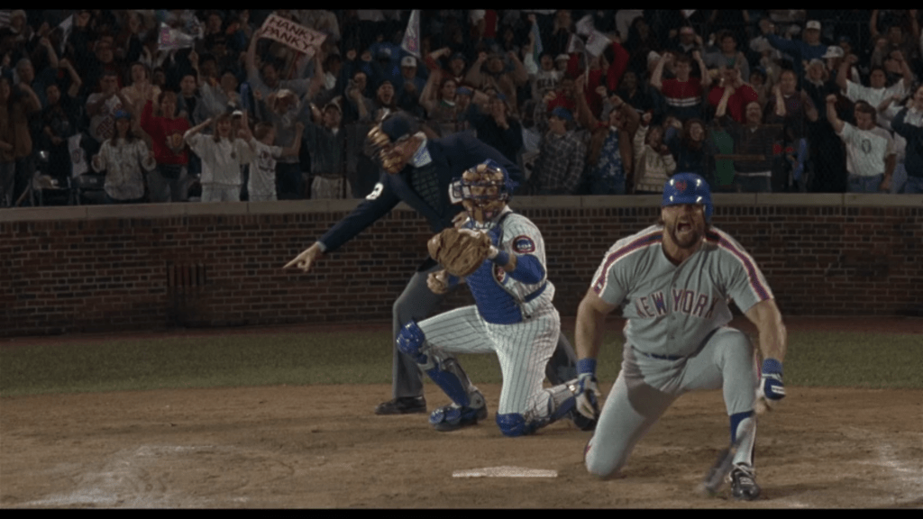 Long shot of an umpire calling a strike behind a catcher getting ready to throw the ball back to Henry behind Heddo howling in disbelief