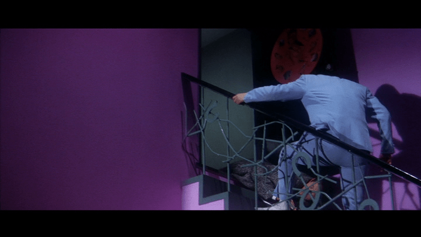 Tetsu opens a door and Yoshii's body falls out on the right side of the frame; the left is dominated by a purple wall