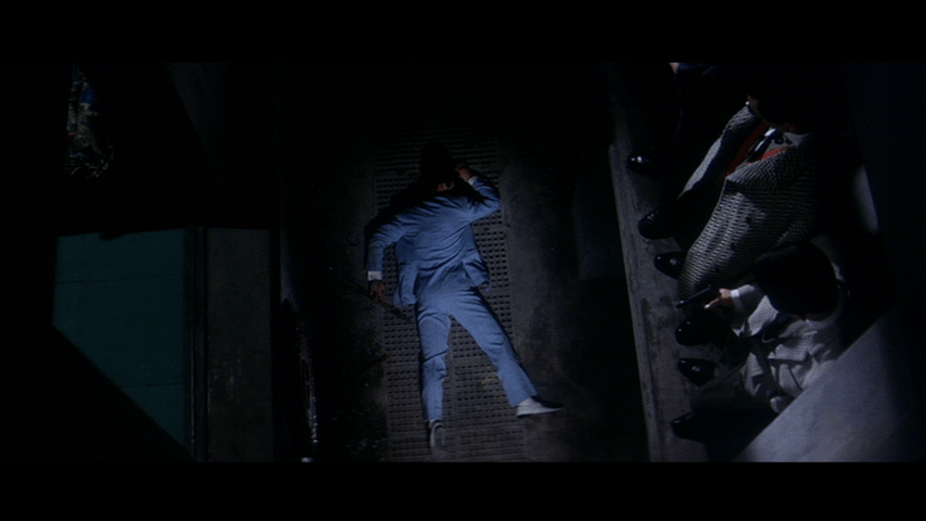 Overhead shot of Tetsu lying unconscious at the bottom of an elevator shaft in the middle of the frame