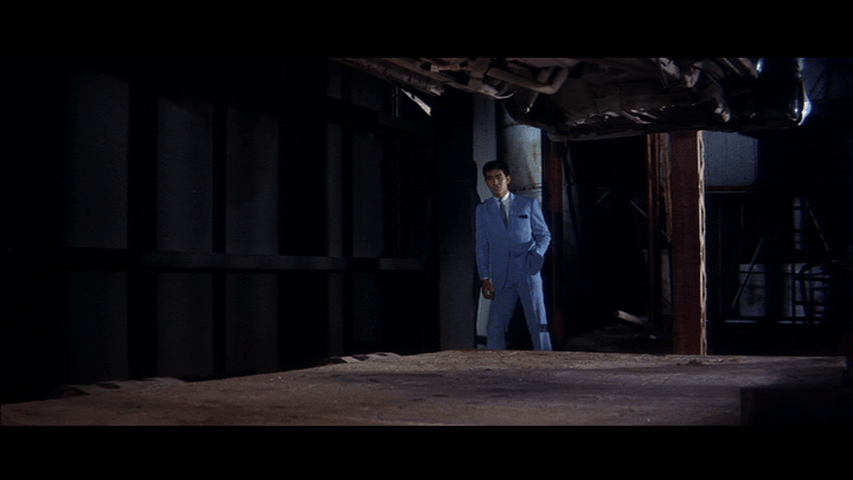 Medium shot of Tetsu in a blue suit singing in the middle of the frame