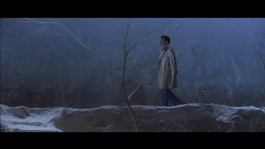 Long shot of Tetsu walking through a snowy landscape singing