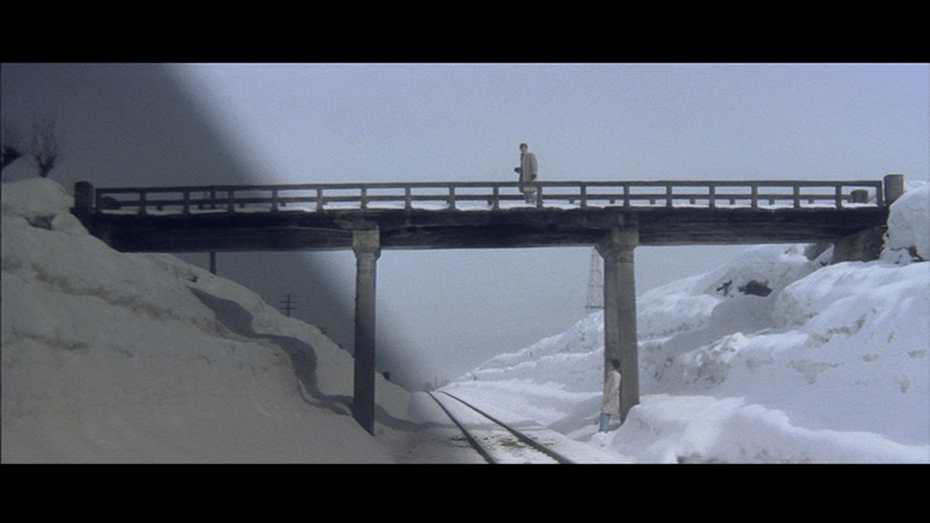 Extreme long shot of Tatsu crossing a bridge while Tetsu watches him from below