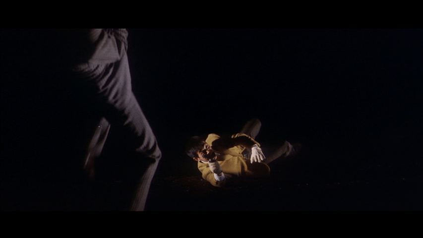 Tetsu dives to the ground and rolls while aiming his gun at a gray-suited figure in the foreground