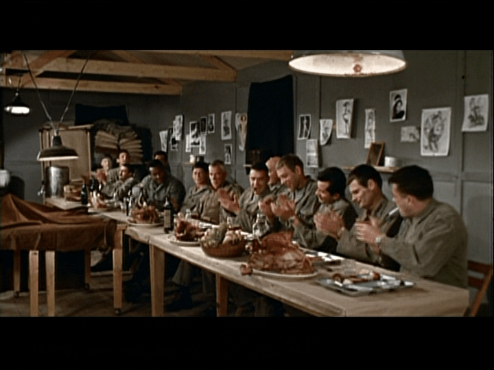 Long shot of the "dirty dozen" sitting at a long table reminiscent of many paintings of the last supper