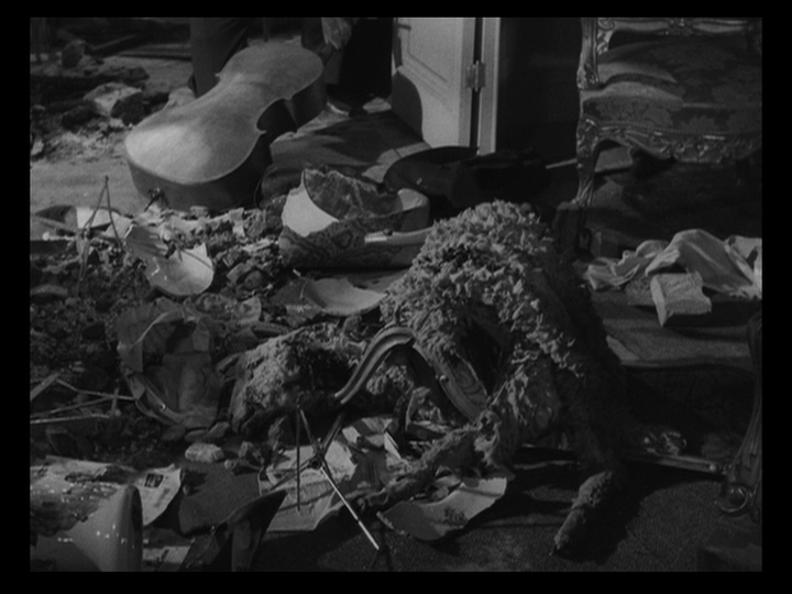 Long shot of a floor strewn with debris, including a cello at the top of the frame