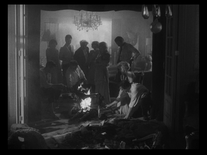 Long shot of the guests huddled around a smoky cookfire, framed by the threshold that they can't cross