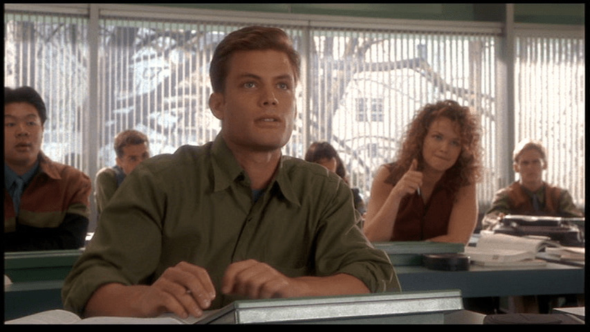 Medium shot of Johnny now looking up at the front of the room