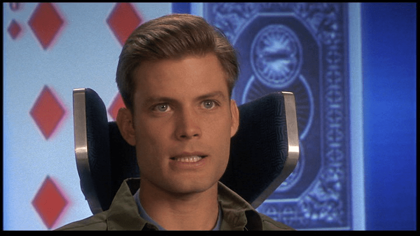 Close-up of Johnny in front of a screen depicting two playing cards, one face down and the other face up