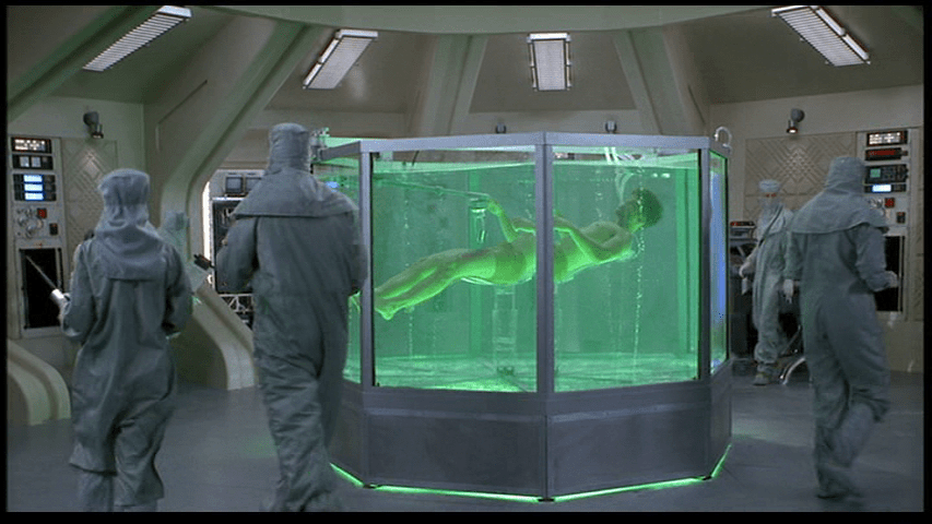 Long shot of Johnny floating in green liquid as his injuries are healed
