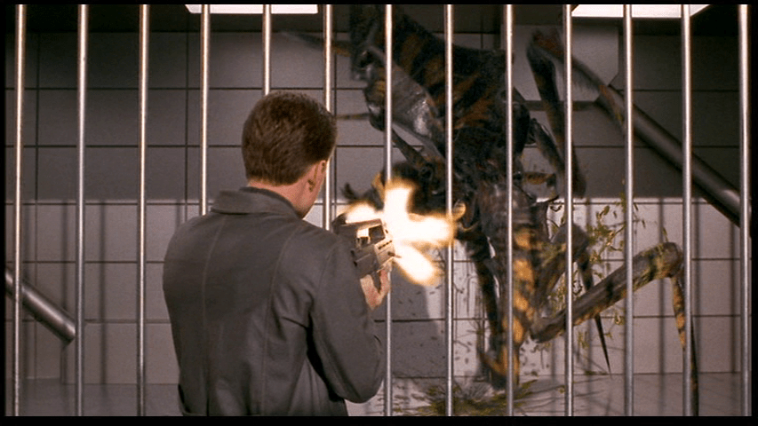 Medium shot of Carl with his back to the camera shooting a Bug prisoner through the bars of its cell