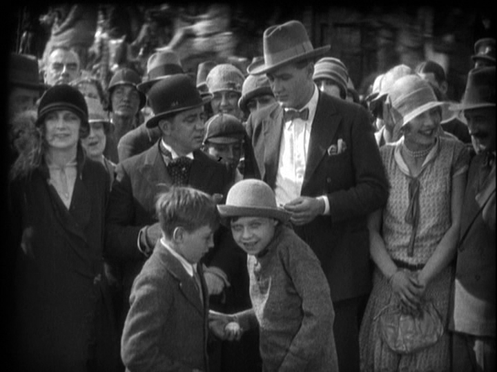 Long shot of two extremely mischievous boys centered in the frame in the foreground of a crowd shot getting ready to throw eggs