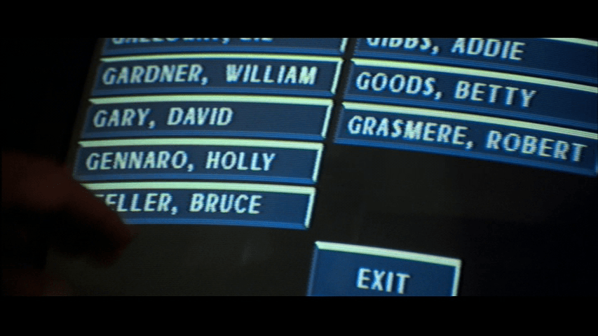 Close-up of a touchscreen directory listing "Holly Gennaro" as an employee of the Nakatomi Corporation