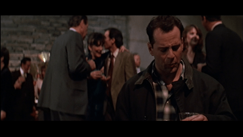 Medium shot of McClane, who occupies the right third of the frame, looking askance at his cup of champagne