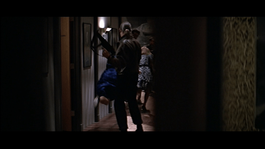 POV medium long shot from McClane's perspective of a man with an automatic weapon taking hostages