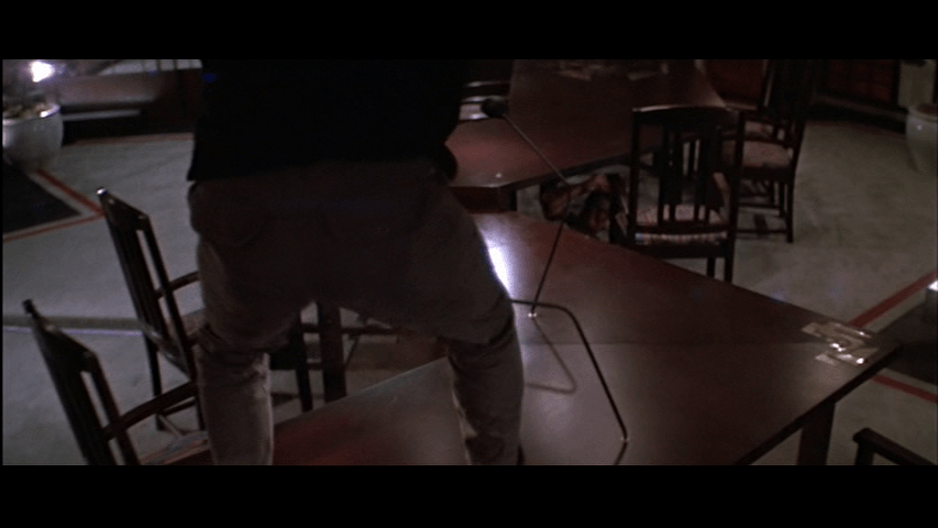 Overhead shot of Marco standing atop a long twisty table with his back to the camera