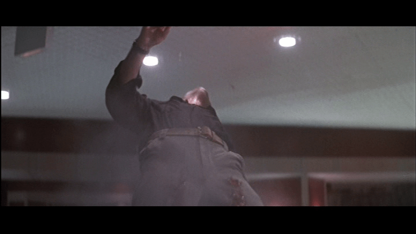 Low-angle shot of Marco falling backwards as McClane shoots him