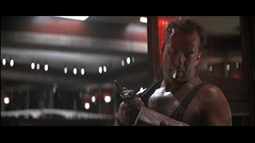 Medium close-up of McClane holding a walkie-talkie and inspecting a block of C4 as he occupies the right third of the frame