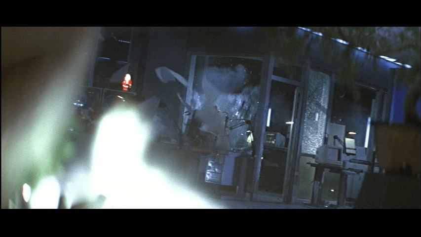 POV shot of the glass box McClane is hiding in from Karl's perspective over the muzzle flare from his gun in the foreground