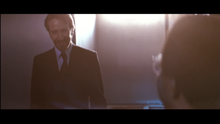 Gruber, bathed in golden light, smiles at Theo, who is out of focus in the right foreground with his back to the camera, from the left half of the frame