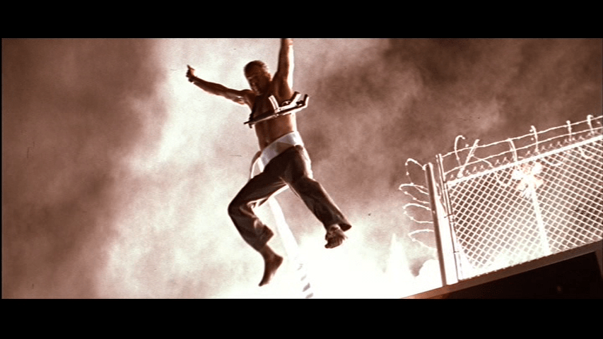 Low-angle shot of McClane leaping off the roof of Nakatomi Plaza with a fire hose tied around his waste just ahead of a massive explosion