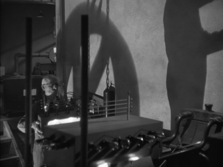Long shot of Clyde Wynant working on an invention in the bottom left quadrant of the frame and casting a huge shadow that occupies the entire right third of it