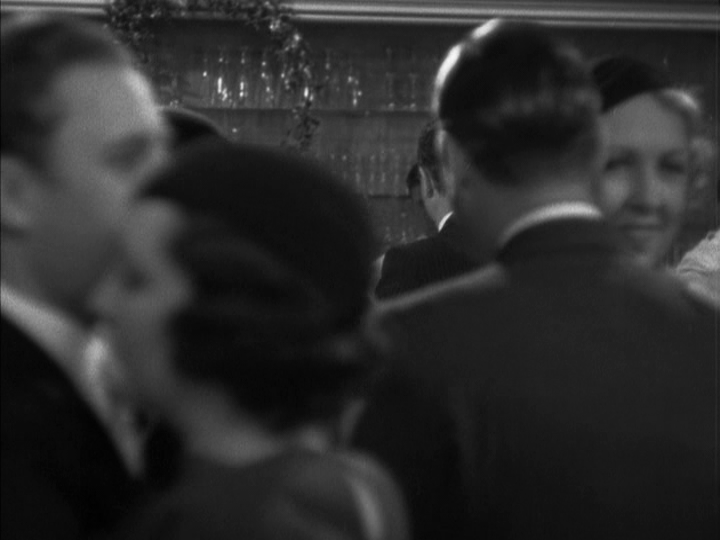 Continuation of the previous image: the people in the previous image are now out of focus in the foreground of the frame, and through them we can just glimpse the profile of Nick Charles