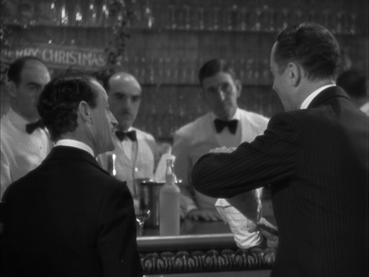 Continuation of the previous image: Nick shakes a drink in the right half of the frame with his back to the camera.