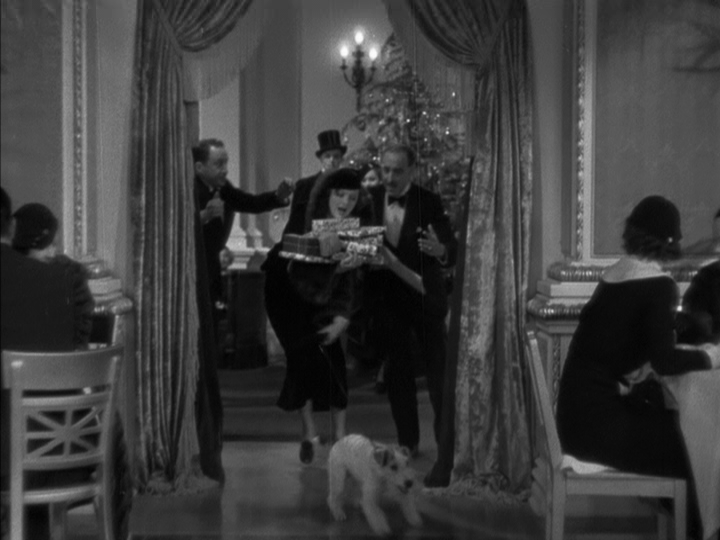 Long shot of a Nora being pulled into the restaurant by Asta as the large pile of presents she carries begins to topple