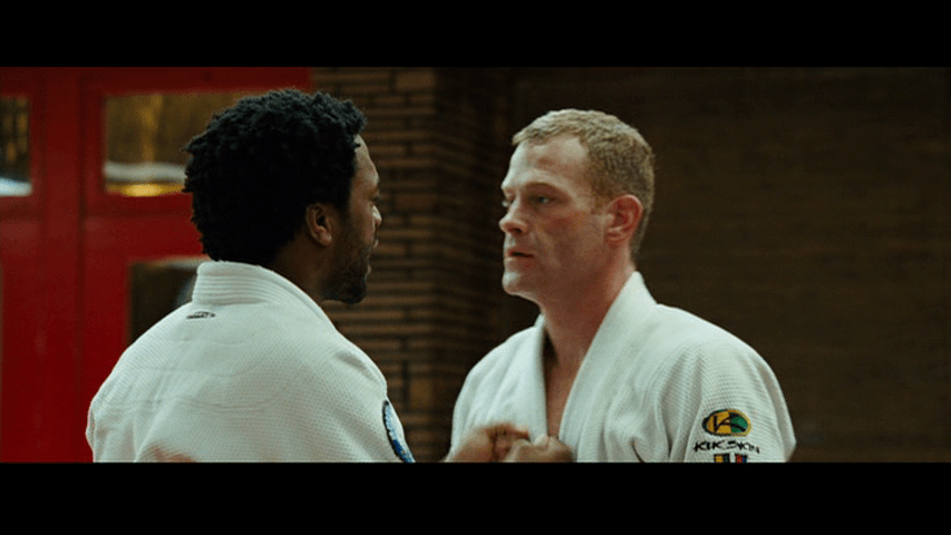 Medium close-up of Mike with his back to the camera, thumping Joe on the chest