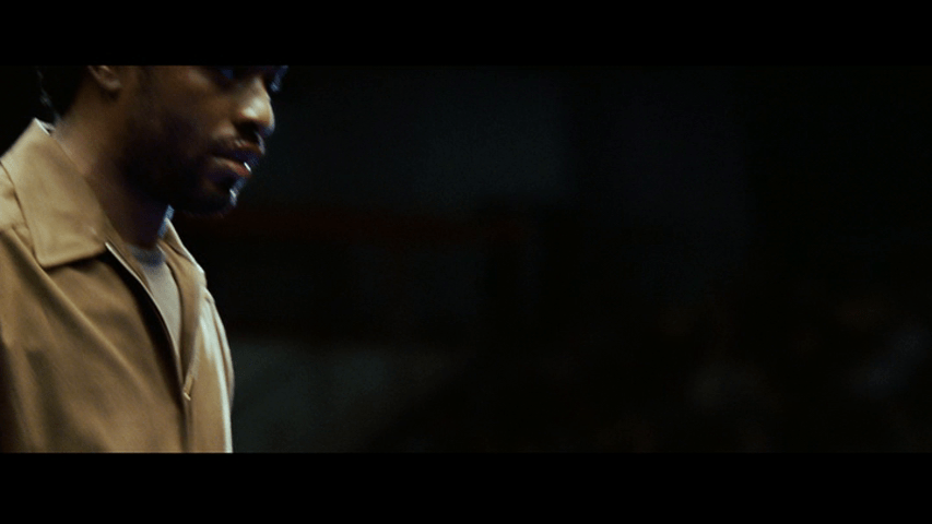 Close-up of Mike, bloodied and set off from a midnight black background in the left third of the frame