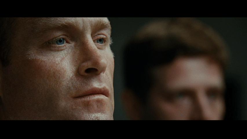 Close-up of a fighter's face in focus in the left side of the frame as another fighter's face occupies the right out of focus