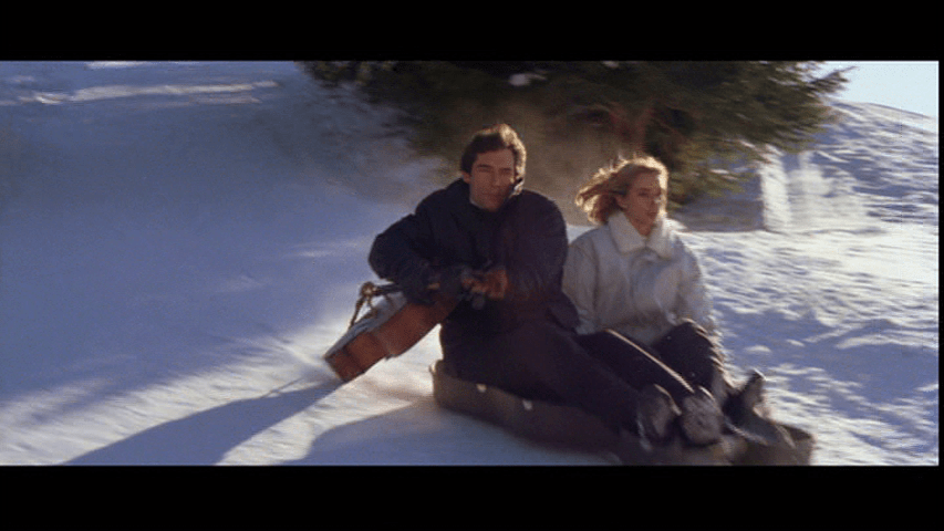 Medium long shot of Bond using the Stradivarius owned by Maryam d'Abo's Kara Milovy to steer its case, which they are using as a sled