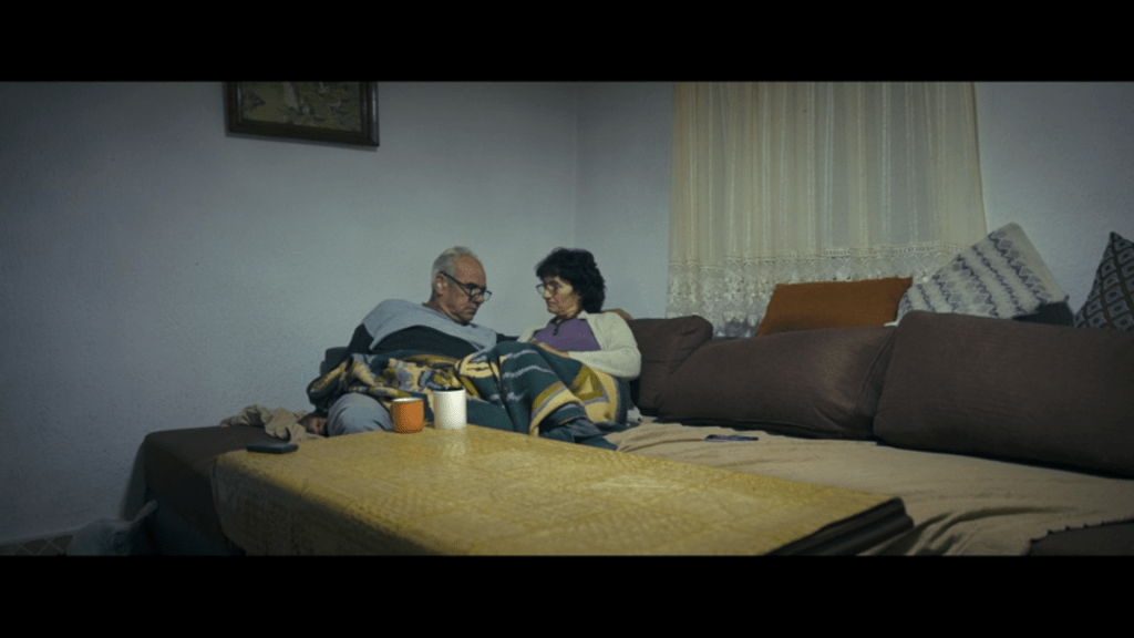 Long shot of Jana and her husband Nikola looking sadly at each other on their couch