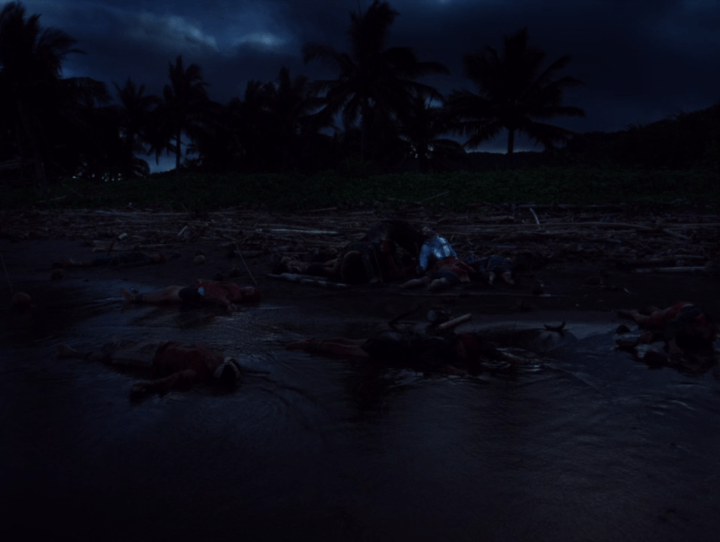 Long shot of a wounded Ferdinand Magellan (Gael García Bernal) in his armor sitting on a beach strewn with dead bodies