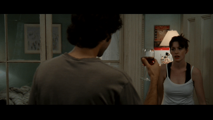 Medium shot of Nate with his back to the camera in the middle of the frame handing a glass of wine to Andy, who approaches from screen right