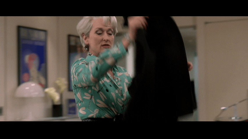 A medium shot of Miranda in a different outfit throwing a different coat on Andy's desk