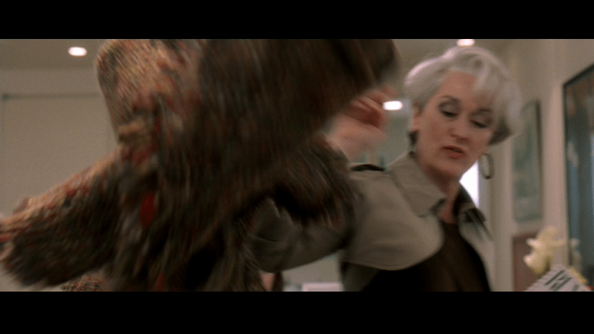 Medium shot of Miranda in yet another outfit throwing yet another coat on Andy's desk