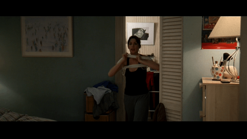 Medium long shot of Andy putting on a second layer as she walks toward the camera from a doorway centered in the frame