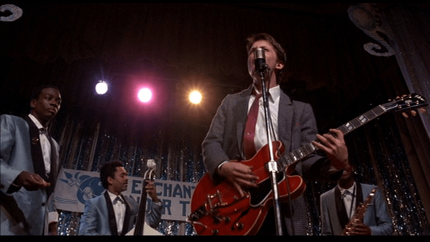 Medium long shot of Michael J. Fox's Marty McFly performing "Johnny B. Goode" backed by Marvin Berry and the Starlighters