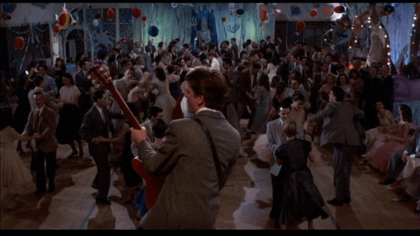 Long shot of Marty rocking out with his back to the camera in the foreground as the kids he's playing for boogie in the background
