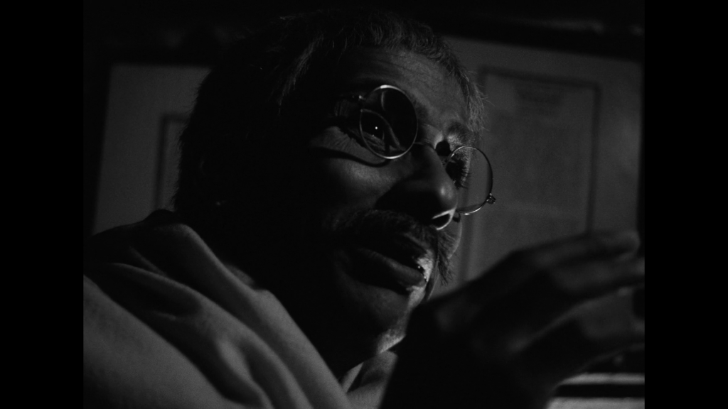 Close-up of Taran facing screen right, his face half-covered in deep shadows