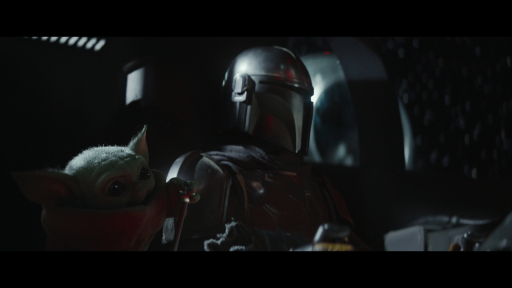 Medium close-up of Grogu grasping the knob on a lever in Din Djarin's spaceship in front of the latter, who does not notice