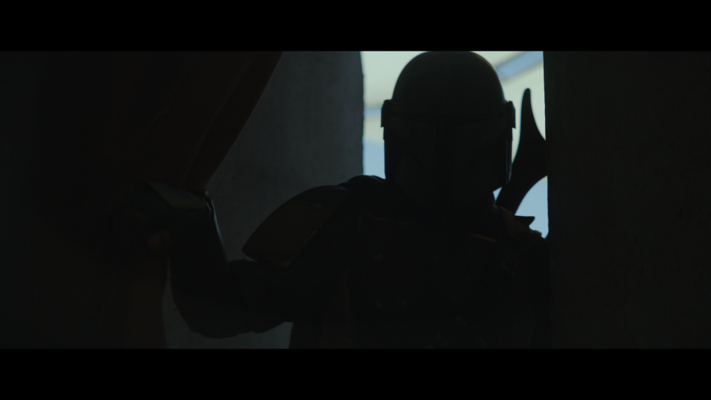 Medium shot of a silhouetted Mandalorian pulling aside a curtain to enter a doorway