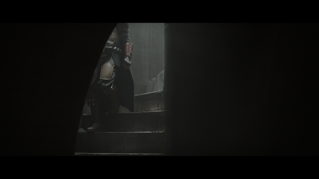 Medium long shot of the Mandalorian's legs and torso as he descends a staircase