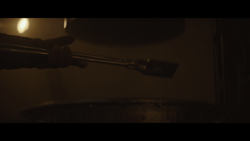 Close-up of the Armorer handling the ingot with tongs