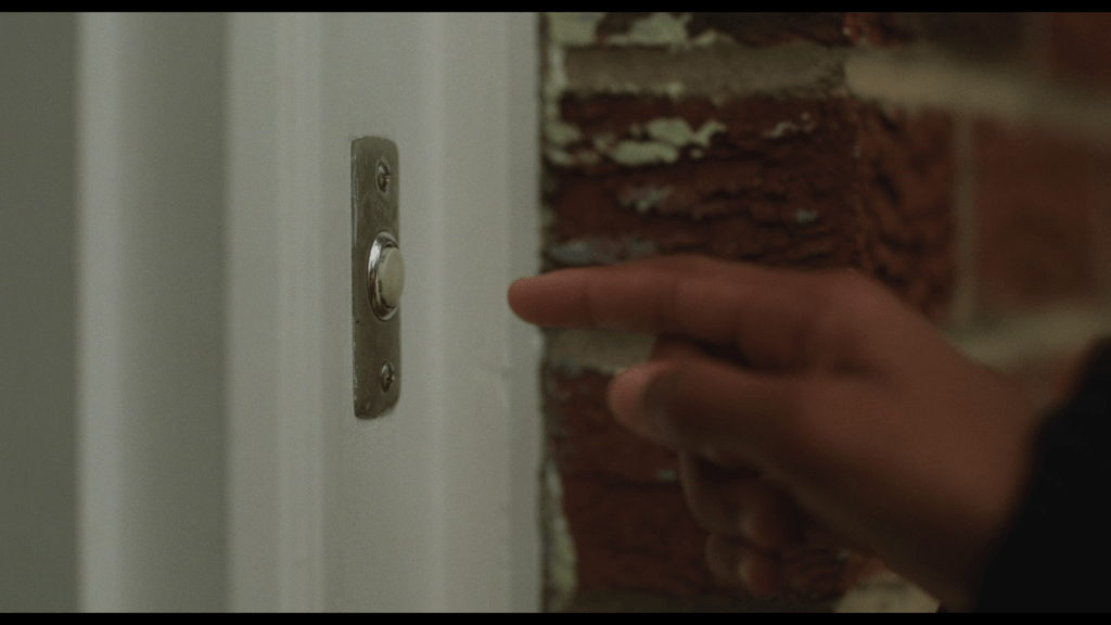 Close-up of Owen's finger hovering over the doorbell of his friend's house